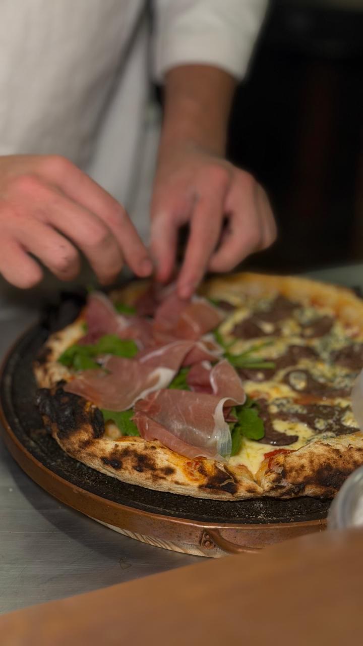 Pizzaiolo colocando presunto parma sobre a Parma e Rúcula recém saída do forno